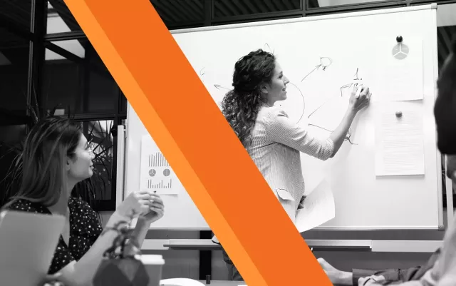 black and white woman writing on whiteboard as colleagues watch