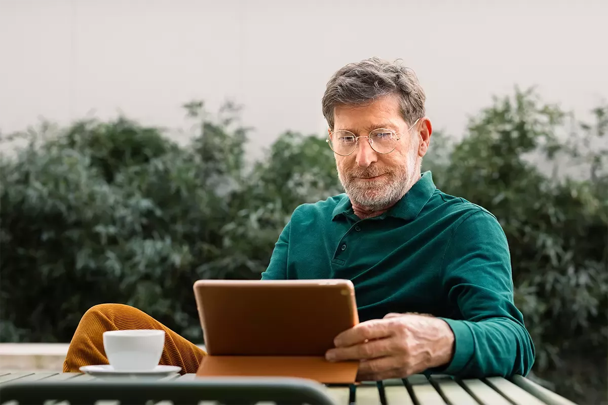 An older man sits outside at a table using a tablet.