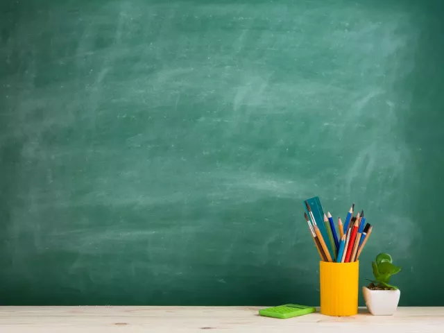 Blank green chalkboard with yellow cup of drawing utensils to the right.