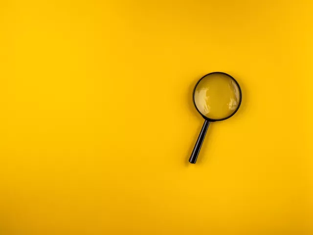 Magnifying glass lies on a yellow background with shadows in the left bottom and top right corners.