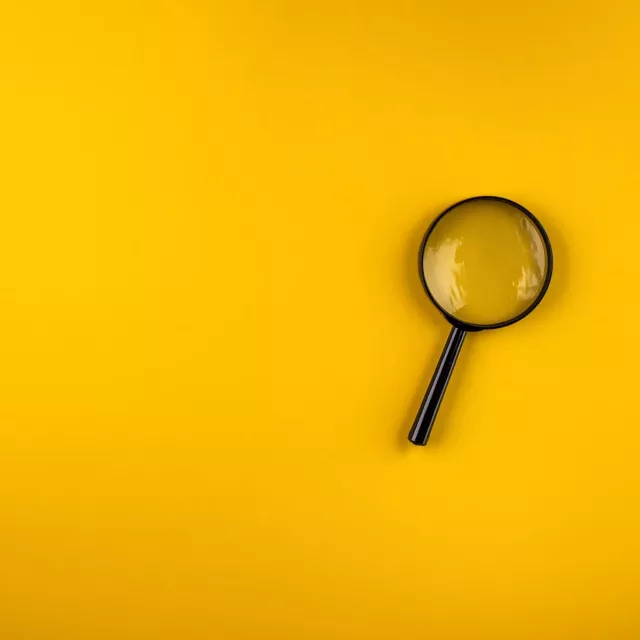 Magnifying glass lies on a yellow background with shadows in the left bottom and top right corners.