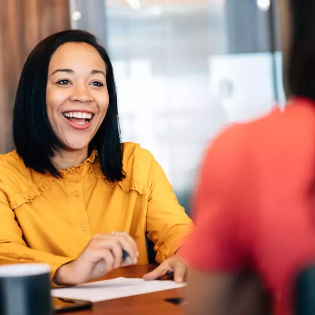 Sales rep laughs while chatting at a desk with sales leadership.