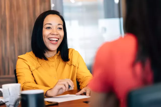 Sales rep laughs while chatting at a desk with sales leadership.