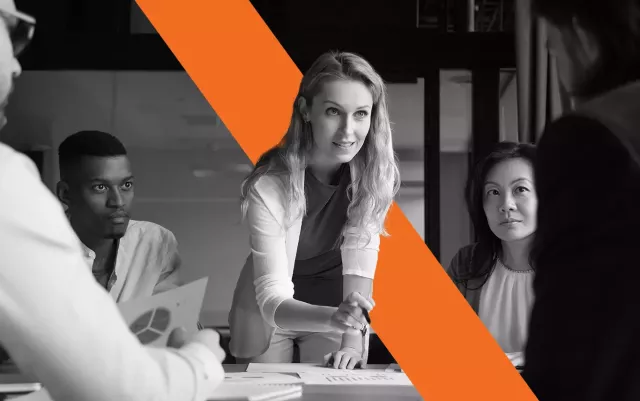 black and white woman leaning over table around a group of people blog header for Xactly