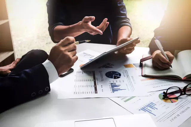 Close up of the torso, arms and hands of business professionals around a conference table reviewing charts and tables.