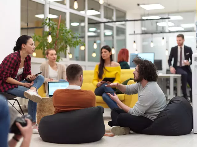 Sales and marketing colleagues at a start-up meet in an open space using quirky seating and laptops.