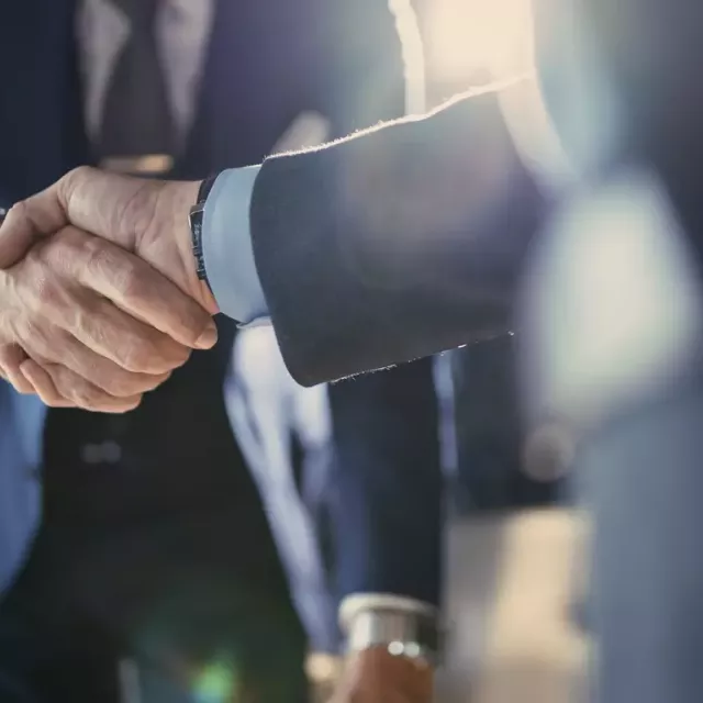 Two businessmen in suits shaking hands in a close of photo not showing their faces with lens flare.