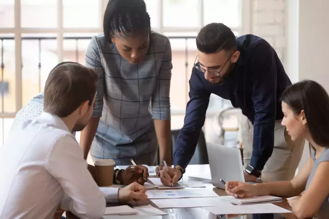 Young professionals wearing business casual clothing discuss sales plans at a conference table.